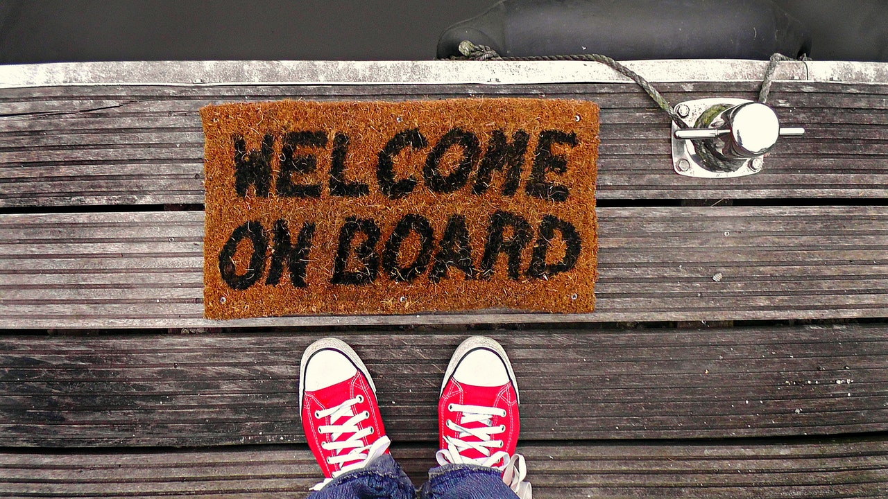 Sneakers in front of a floor mat with the words, 'WELCOME ON BOARD'